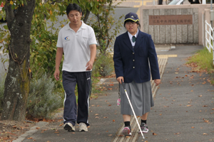 生徒が歩行訓練の資格をもった教員に見守られながら白杖を使っての歩行訓練を行っています。