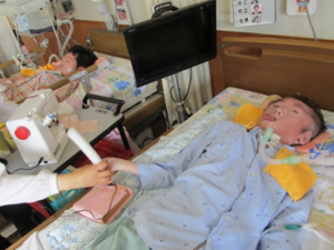 病院内のベッド上で生徒がIct機器を使って授業を受けています。