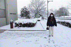 雪の降り積もった中，学校の前で立っています。とても寒そうです