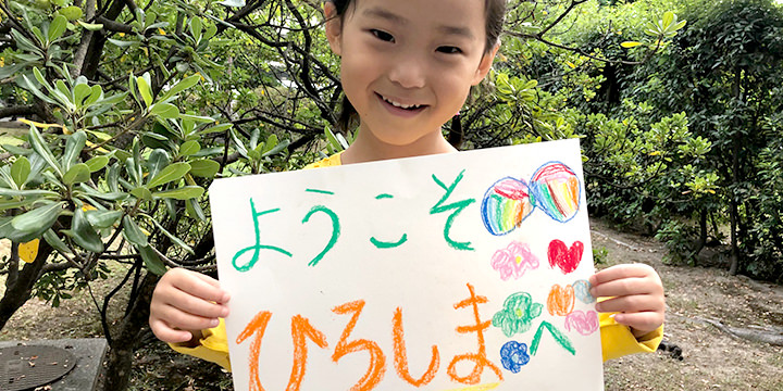 歓迎メッセージを書いた紙を掲げる少女
