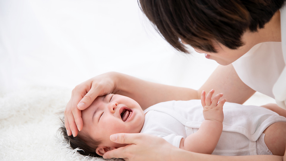 赤ちゃんのおでこに手を当てる女性