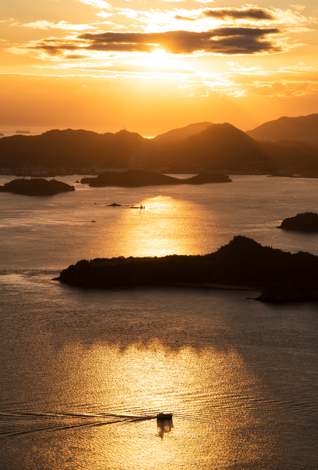 夕日が沈む海と島々と船が航行している写真
