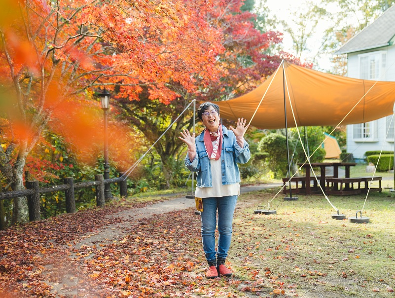 紅葉がきれいなユースホステルの敷地で両手を広げて微笑む女性