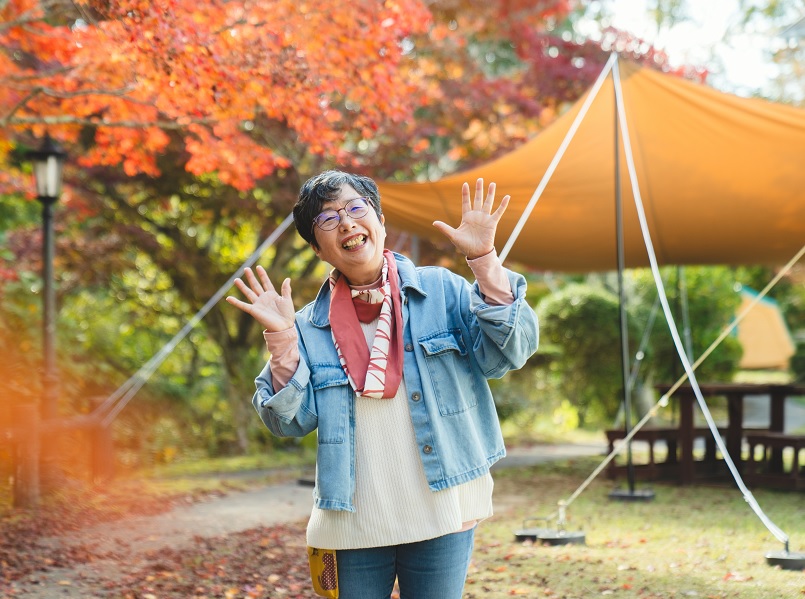 紅葉がきれいな背景で両手を広げ微笑む女性