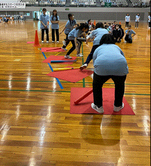 障害物競争の競技で学生がバットを頭につけて回転している。