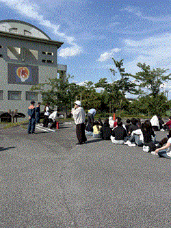 学生が避難後に集合して消防のかたから説明を受けている
